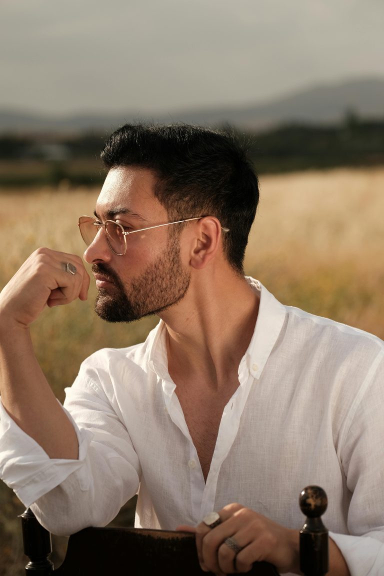 Stylish man in a field wearing a white shirt, contemplating at sunset.